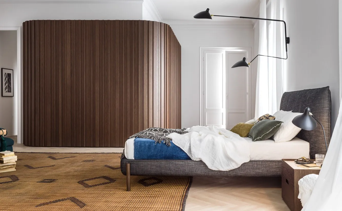Armario Stave con puertas batientes de listones y lateral curvo en un dormitorio.