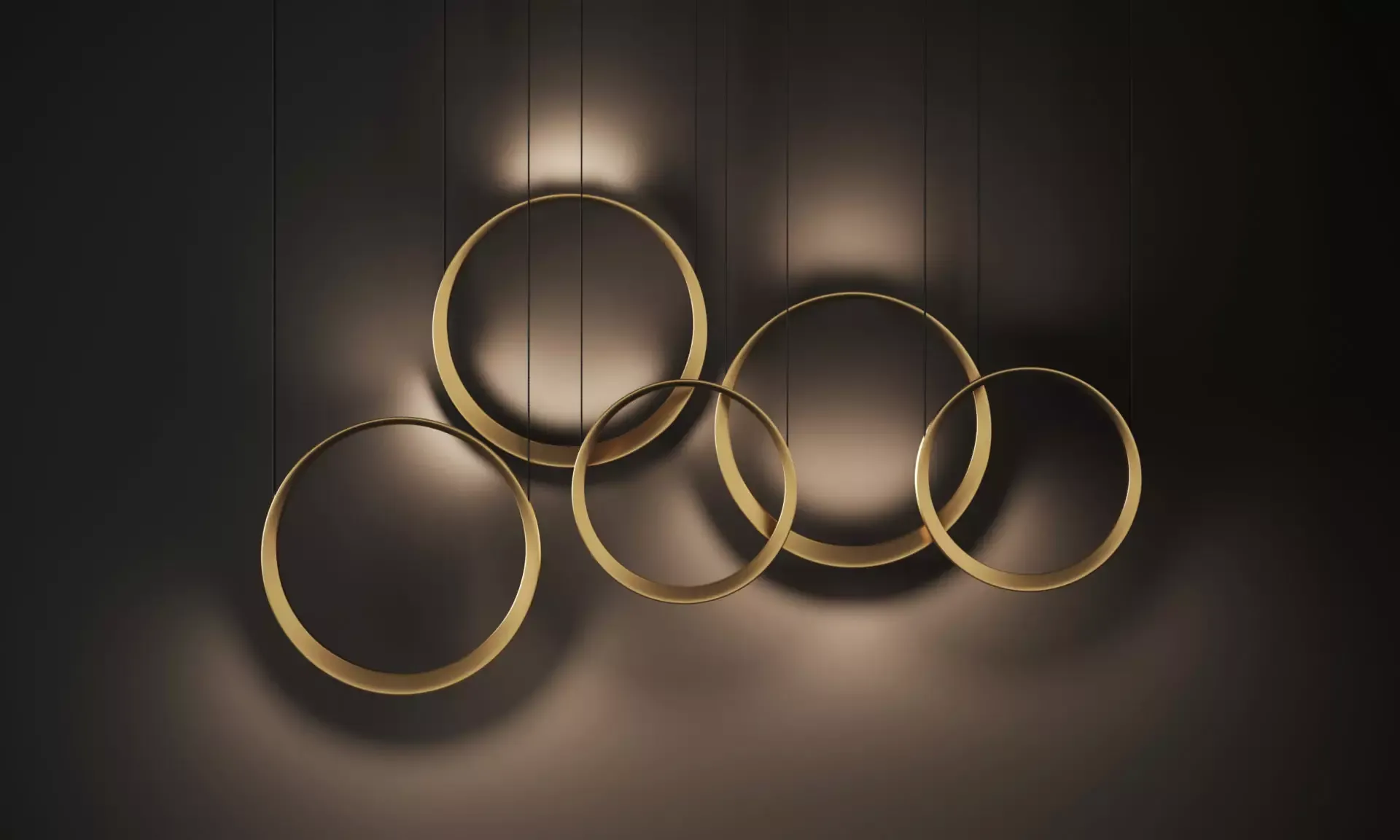 Five brass Quasar Moonlight rings on a dark wall